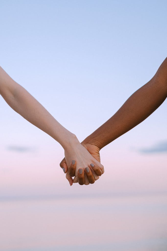 Closeup of multiracial hands holding, symbolizing unity and equality against a serene sky.